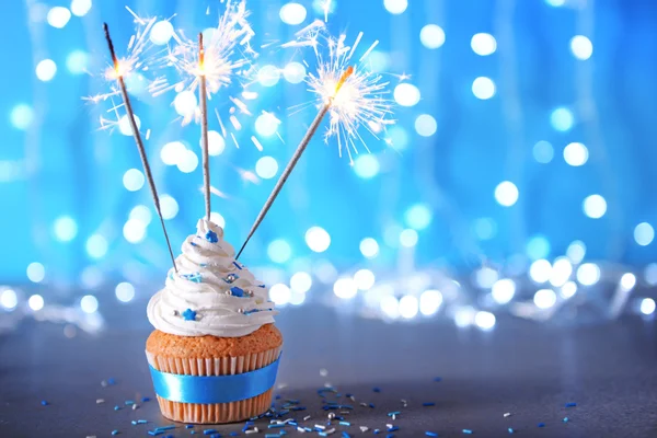 Cupcake con glaseado de crema blanca y bengalas sobre un fondo brillante —  Fotos de Stock