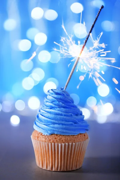 Cupcake mit blauer Sahneglasur und Wunderkerze auf glitzerndem Hintergrund, Nahaufnahme — Stockfoto