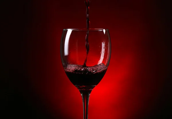 Wine pouring in glass on dark red background — Stock Photo, Image