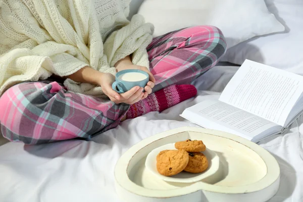 Mujer en pijama leyendo un libro y bebiendo leche en su cama — Foto de Stock