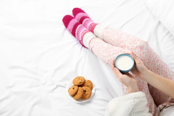 Frau im Schlafanzug hält Tasse Milch auf ihrem Bett — Stockfoto