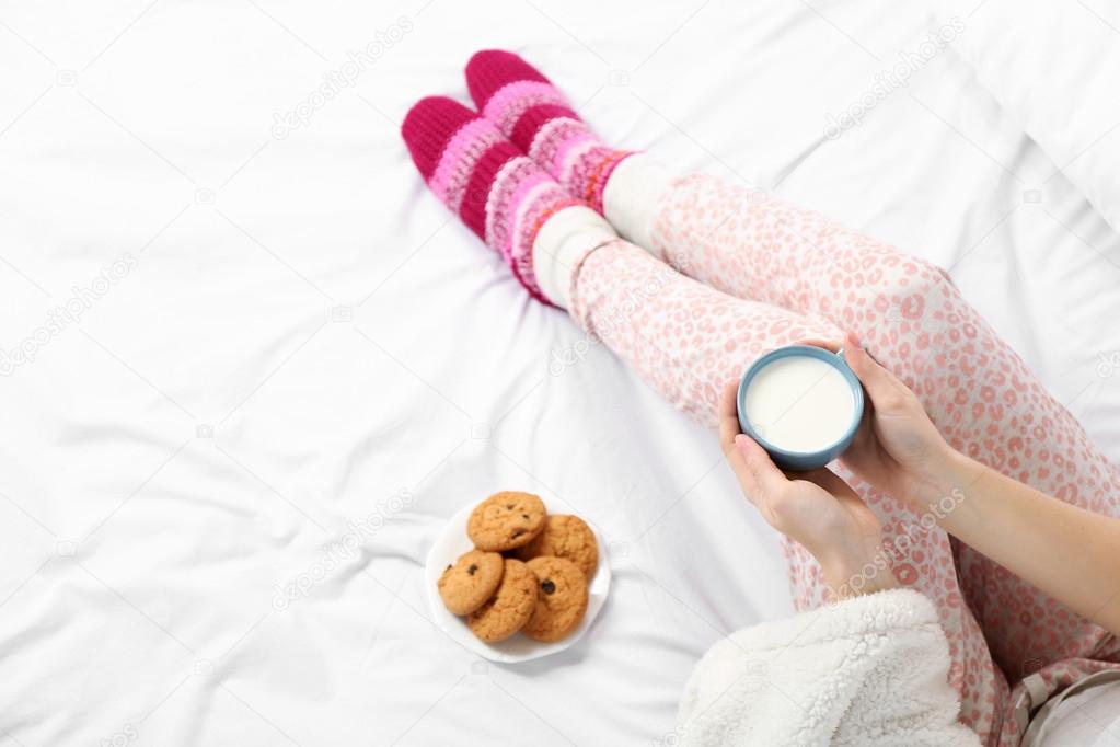 Woman in pajamas holding cup of milk on her bed