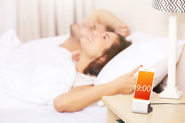 Couple waking up with mobile alarm clock — Stock Photo, Image