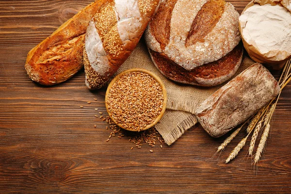 Pane appena sfornato e una ciotola di chicchi di grano sullo sfondo di legno — Foto Stock