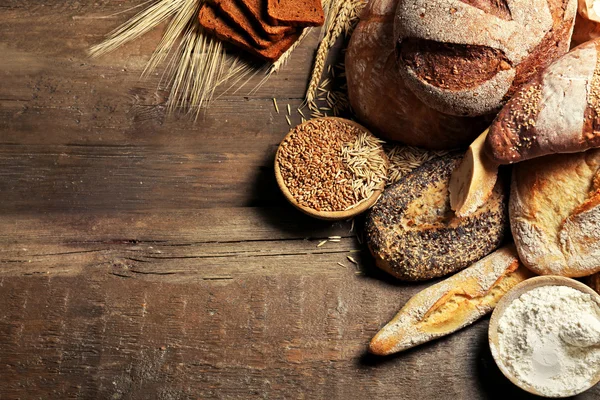 Pão fresco assado, farinha e trigo no fundo de madeira — Fotografia de Stock