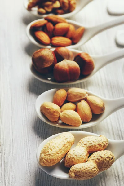 Nueces, almendras, avellanas, pistachos y cacahuetes en las cucharas de cerámica en la mesa de madera, primer plano —  Fotos de Stock