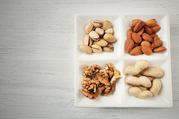 Nueces, almendras, pistachos, cacahuetes en la placa rectángulo de cerámica en la mesa de madera —  Fotos de Stock