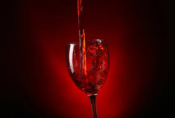 Вино наливается в стекло на темно-красном фоне — стоковое фото