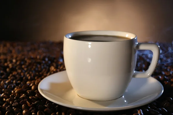 Kop warme koffie onder koffie bonen op donkere achtergrond — Stockfoto
