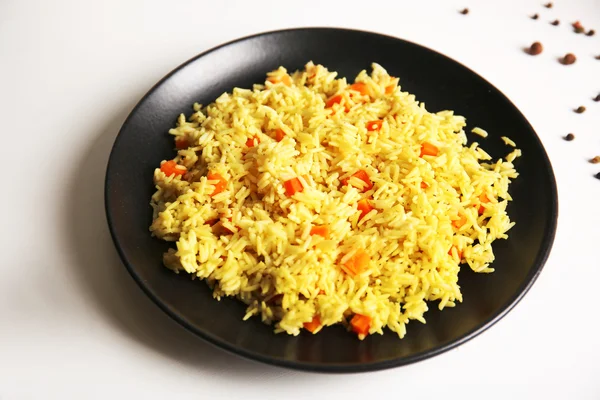 Stewed rice with a carrot on a black plate, close up — Stock Photo, Image