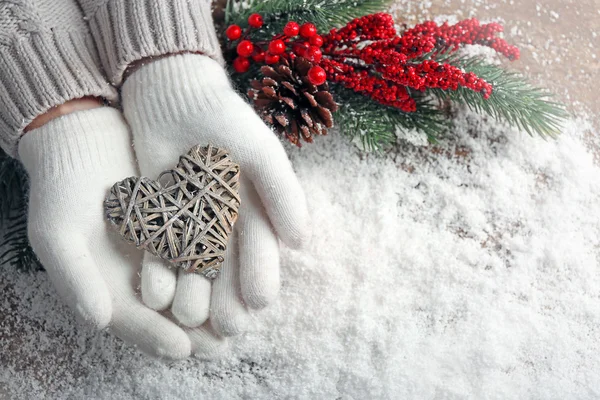 Frauenhände in Fäustlingen mit dekorativem Herz auf Schnee-Hintergrund — Stockfoto