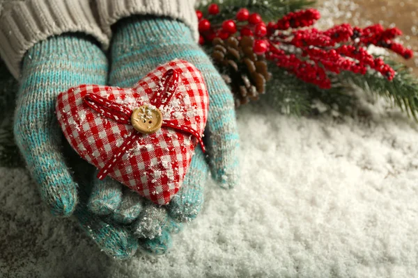 Vrouwelijke handen in blauwe wanten met decoratieve hart op sneeuw achtergrond — Stockfoto