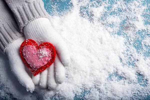 Mãos femininas em mitenes com coração decorativo no fundo da neve — Fotografia de Stock