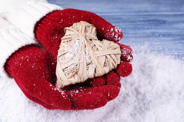 Mains féminines en mitaines avec coeur décoratif sur fond de neige — Photo