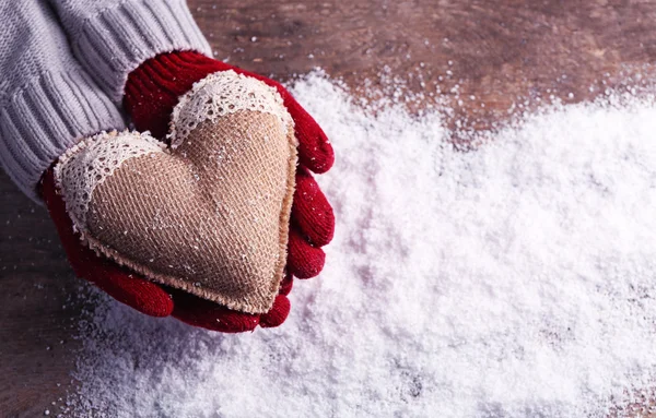 Manos femeninas en manoplas con corazón decorativo sobre fondo de nieve —  Fotos de Stock