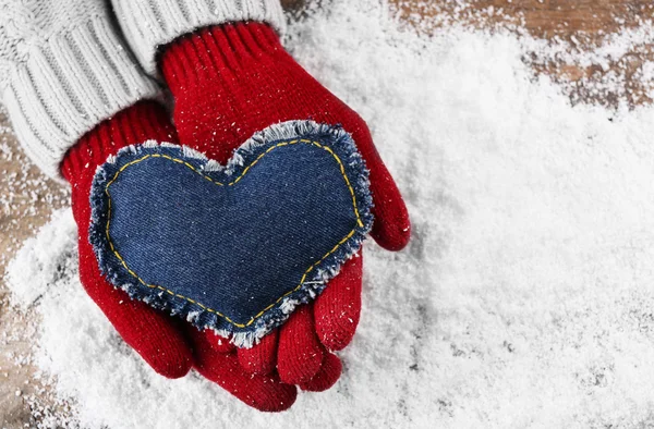 Vrouwelijke handen in wanten met decoratieve hart op sneeuw achtergrond — Stockfoto