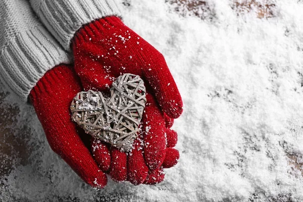 Manos femeninas en manoplas con corazón decorativo sobre fondo de nieve —  Fotos de Stock