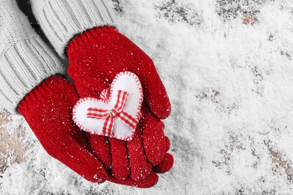 Manos femeninas en manoplas con corazón decorativo sobre fondo de nieve — Foto de Stock