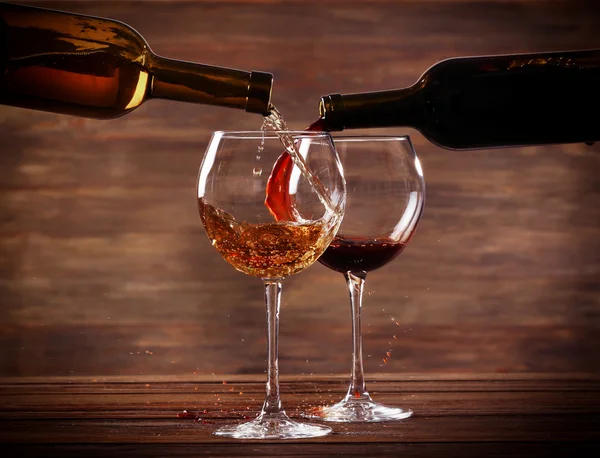 Vin blanc et rouge versant dans des verres sur fond en bois — Photo