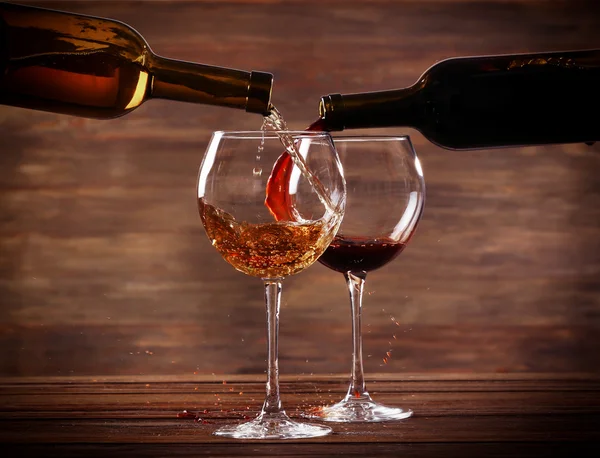 Vino blanco y tinto vertiendo copas sobre fondo de madera — Foto de Stock