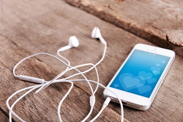 Bílý mobilní telefon s romantický spořič obrazovky a sluchátka na dřevěné pozadí — Stock fotografie