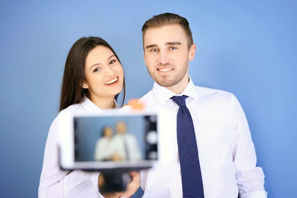 年轻男子和妇女在蓝墙背景下用智能手机制作自己的照片 — 图库照片