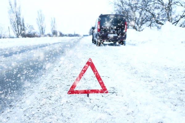 Carro na estrada de inverno e triângulo de aviso — Fotografia de Stock