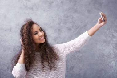 Ona kendini fotoğraf gri duvar arka plan üzerinde çekici kıvırcık saçlı genç kız