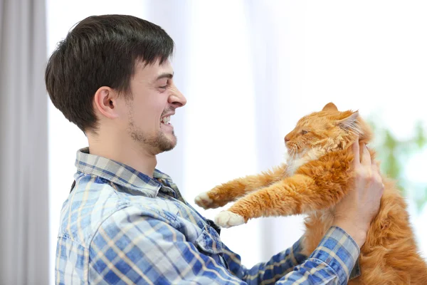Homem irritado segurando um gato rad fofo — Fotografia de Stock