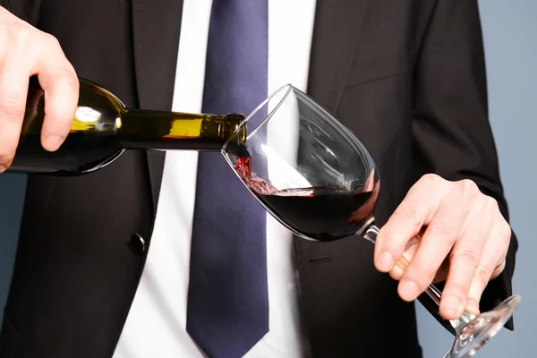 Człowiek w garniturze wylewanie czerwonego wina do kieliszka — Zdjęcie stockowe