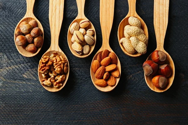 Lepels met hazelnoten, walnoten, pistachenoten, amandelen, eikels en pinda's, op grijze houten achtergrond — Stockfoto
