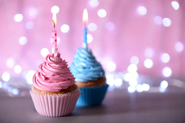 Glitter arka plan üzerinde mum ile iki cupcakes — Stok fotoğraf