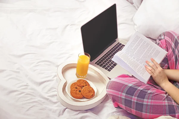Mujer en pijama con portátil leyendo un libro — Foto de Stock