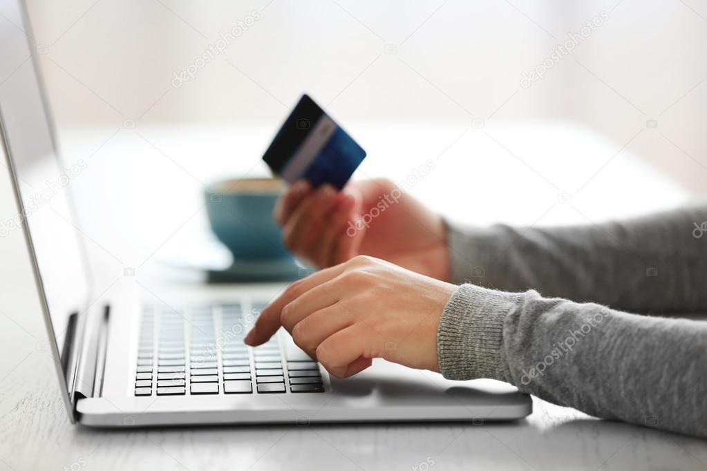 E-commerce concept. Woman with credit card, laptop and cup of coffee, close up