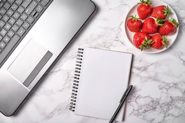 Dizüstü bilgisayarı aç, boş defter, masada çilek ve kalem, kopyalama alanı. Freelancer çalışma alanı, merkez ofis. Üst manzara, düz uzanma