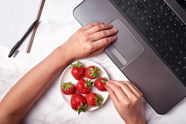 Kadın elleri dizüstü bilgisayarda klavye ve çilekleri masada yazıyor, boşluğu kopyala. Freelancer çalışma alanı, merkez ofis. Üst manzara, düz uzanma