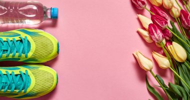 Bir çift spor ayakkabı, bir şişe su ve pembe renkli sarı laleler. Yeni ayakkabılar, fotokopi alanı. Koşu ayakkabılarının üstünden. Üst manzara, düz uzanma