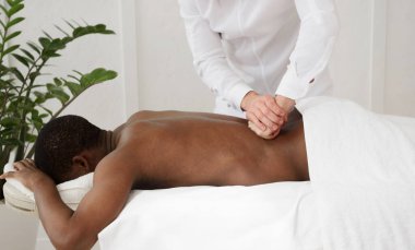 Beyaz arka planda sırt masajı yaptıran Afrikalı Amerikalı bir adam. Boşluğu kopyala, kapat