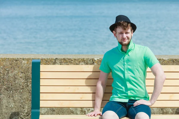 Hipster młody człowiek siedzi na ławce w pobliżu morza odkryty — Zdjęcie stockowe
