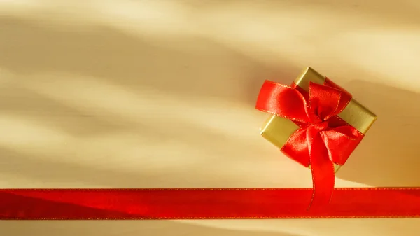 Kleine goldene Schachtel mit Geschenk gebunden rote Schleife — Stockfoto
