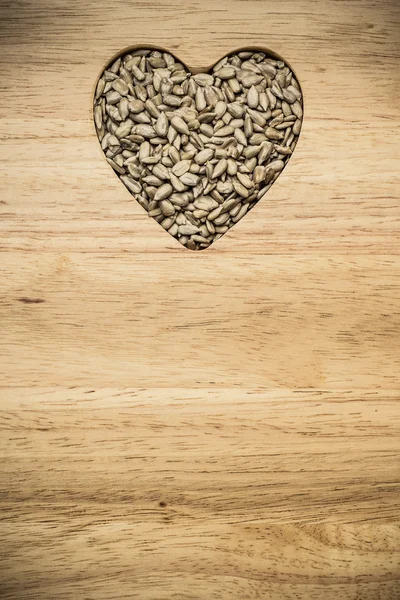 Slunečnicová semínka na povrch dřeva ve tvaru srdce — Stock fotografie