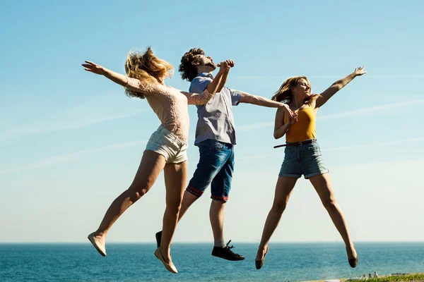 Carefree friends jumping by sea ocean water.