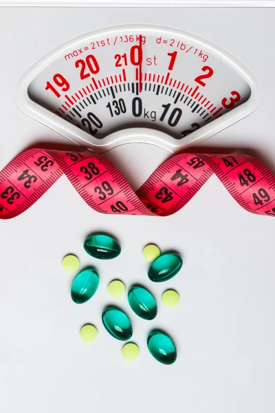 Pills with measuring tape on white scales — Stock Photo, Image