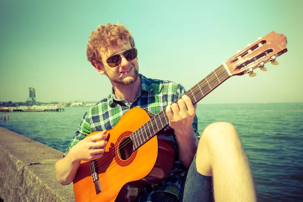 Joven hipster tocando la guitarra por mar océano . — Foto de Stock