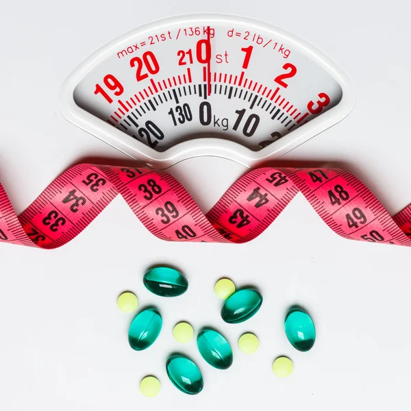 Pills with measuring tape on white scales — Stock Photo, Image