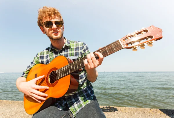 Giovane hipster suonare la chitarra dal mare oceano . — Foto Stock