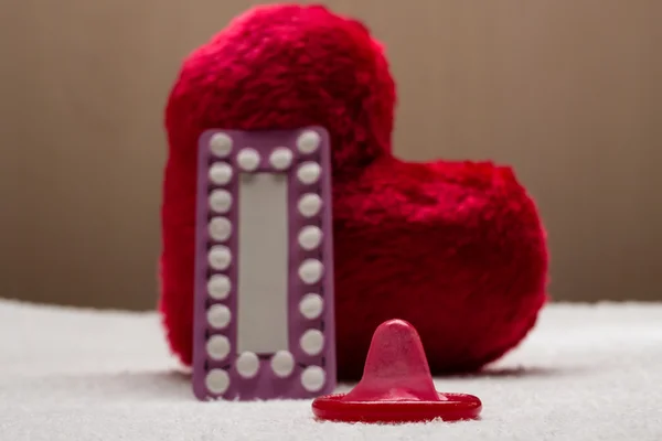 Pillole contraccettive orali preservativo sul cuore rosso — Foto Stock