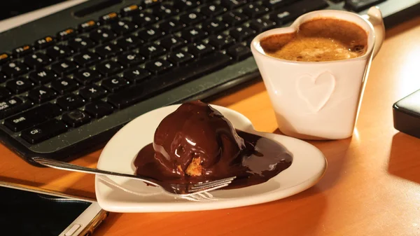 Φλιτζάνι καφέ και σοκολάτας κέικ δίπλα στον υπολογιστή. — Φωτογραφία Αρχείου