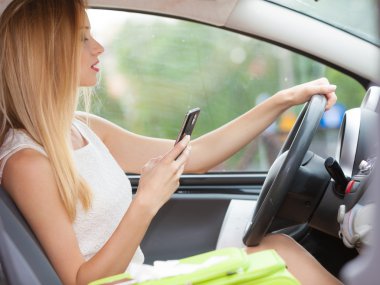 Arabasını kullanırken telefonu kullanan bir kadın.