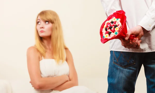 Man with candy bunch flowers and unhappy woman. — Stock Photo, Image